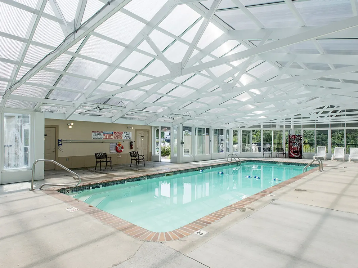 An inviting indoor swimming pool with a transparent ceiling that lets in abundant natural light. The pool is surrounded by a seating area, evoking a tranquil and relaxing atmosphere, and shows the year-round availability for guests.