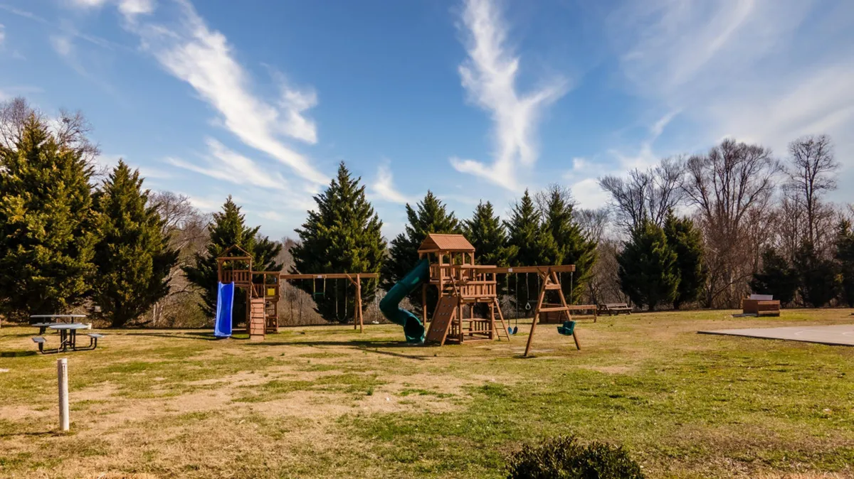 A cheerful outdoor playground with vibrant equipment, green grass, and surrounding trees. Children can be seen playing, and the setting conveys a sense of joy and communal family fun.