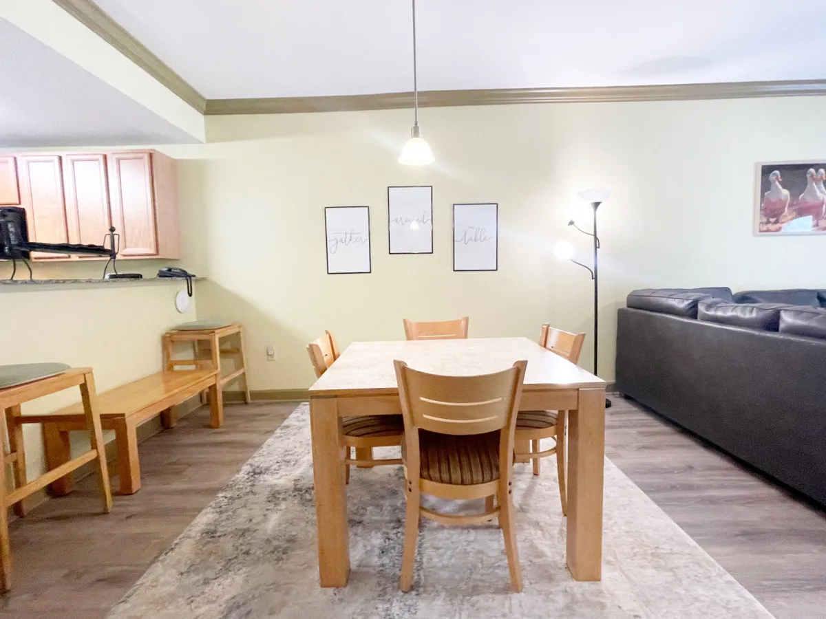 This image features a central dining table with comfortable seating, complemented by wall art and a view of the adjacent kitchen bar. The inviting arrangement is ideal for family dinners, game nights, or shared meals, with an overall atmosphere of warmth and togetherness.