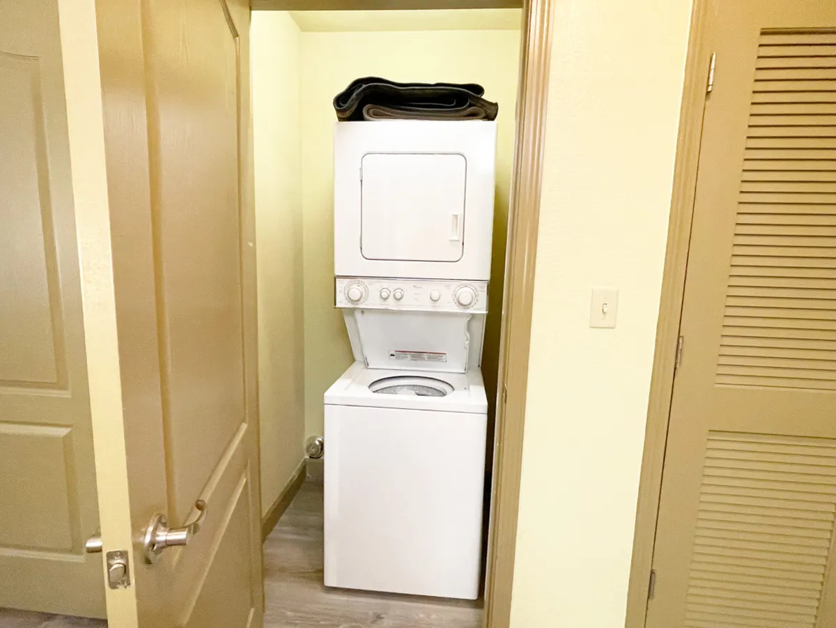 This image shows a practical laundry nook with a stacked washer and dryer and a blanket placed on top. The compact arrangement maximizes convenience and makes laundry tasks quick and easy.