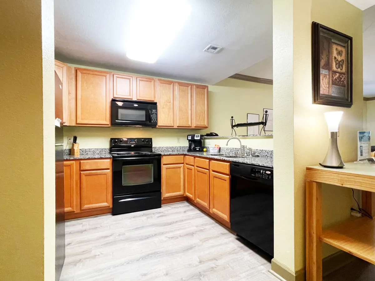 A warm kitchen scene featuring granite countertops, black appliances, wooden cabinets, and a kitchen island. The space is clearly designed for meal preparation and family gatherings, inviting culinary creativity and comfortable entertaining.
