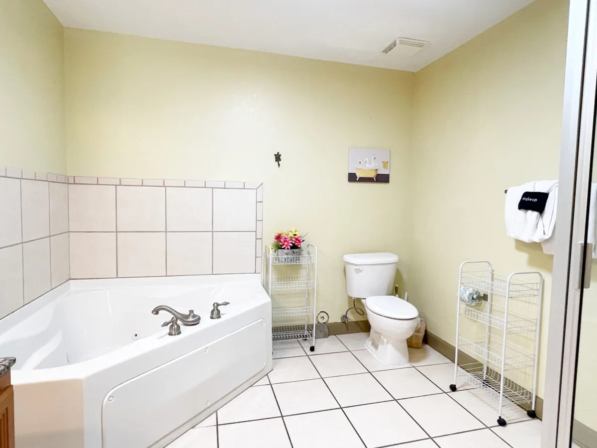 A tranquil bathroom with a large jacuzzi (garden) tub, a separate shower enclosure, a sink area adorned with flowers, and a toilet. The space feels spa-like and is styled for relaxation and self-care.