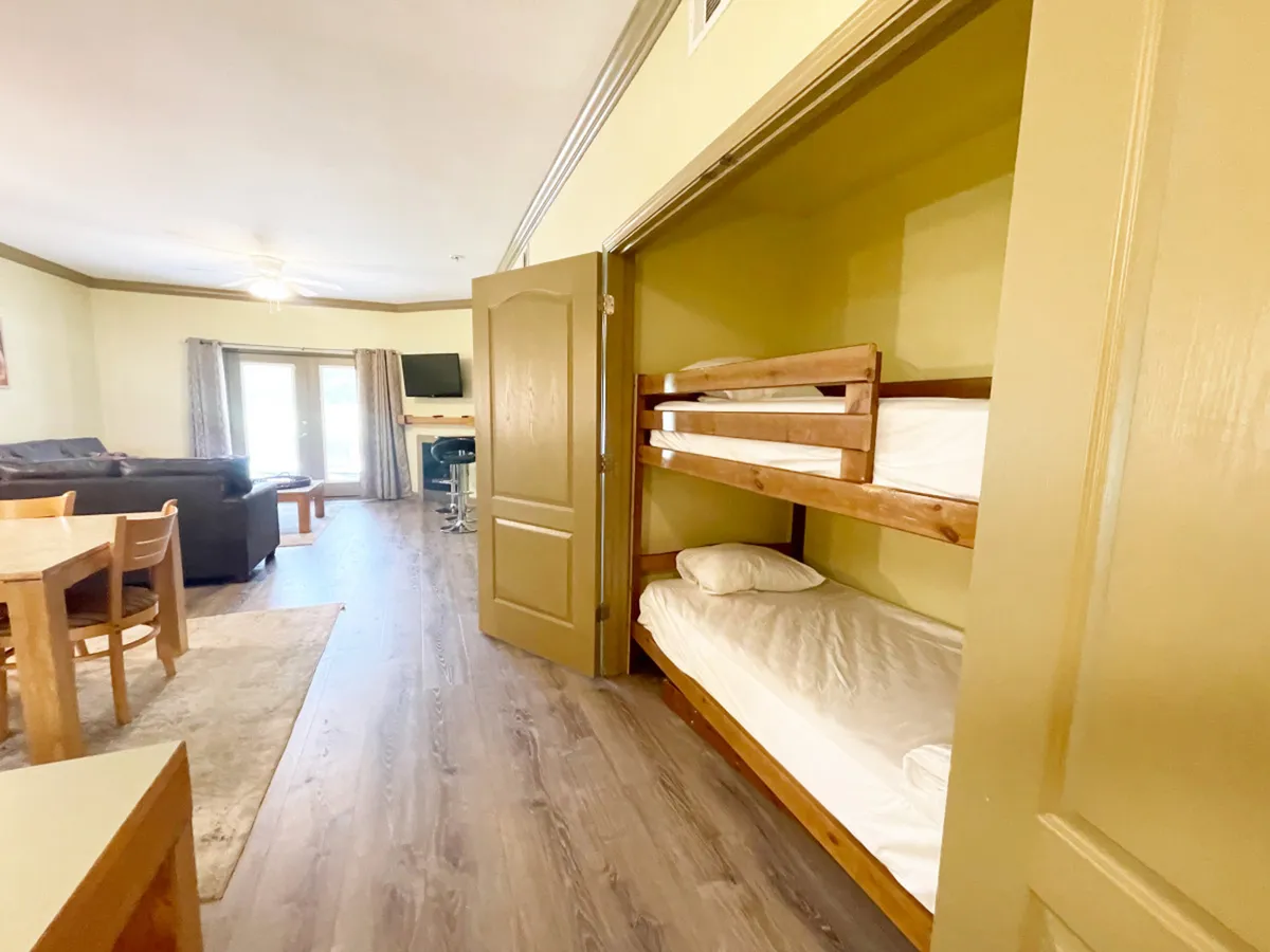 This image features a cozy living space with a dining table, a sofa, and a set of bunk beds visible in the background. The arrangement encourages family gatherings, shared meals, and group relaxation, and clearly displays the unique 'bunk closet' area.