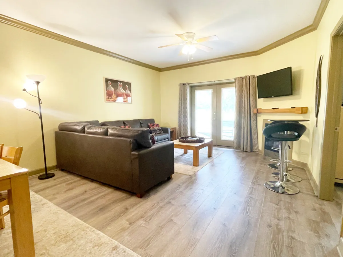 This image showcases a cozy living room with a comfortable sofa, a central coffee table, a large TV, and sliding doors that likely open to a patio or outdoor space. The room is arranged for socializing and relaxing, with plenty of natural light hinting at access to the outdoors.