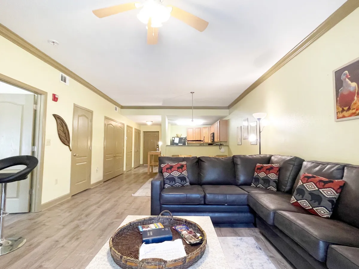 A spacious living area with a leather sectional sofa and a coffee table, with the kitchen visible in the background. Decorative wall art adds warmth and style, and the setup is ideal for relaxing, entertaining, or gathering as a family.